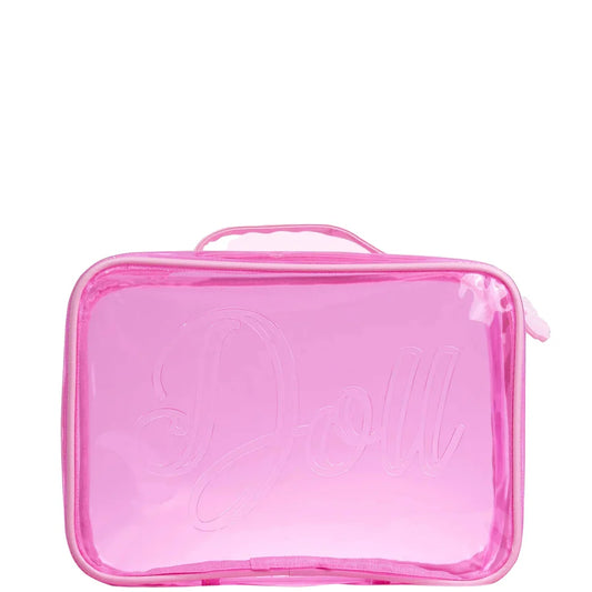 Clear pink Doll Beauty makeup bag with top handle, butterfly zip pulls, and "Doll" embossed on the front, displayed on a wooden stool against a brick wall background.